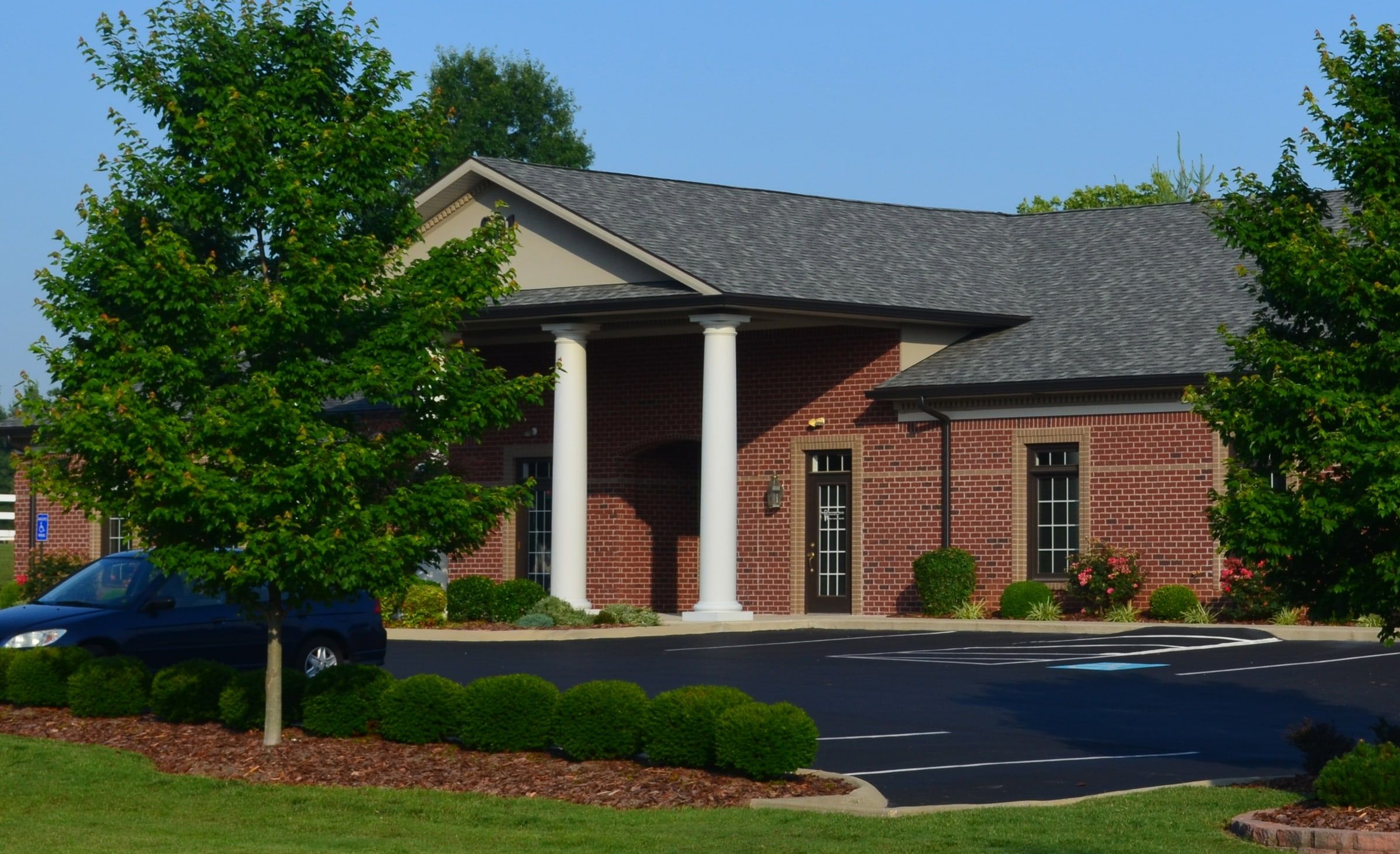 The building at 901 Wilkinson Trace in summer: red brick, white columns and a green lawn