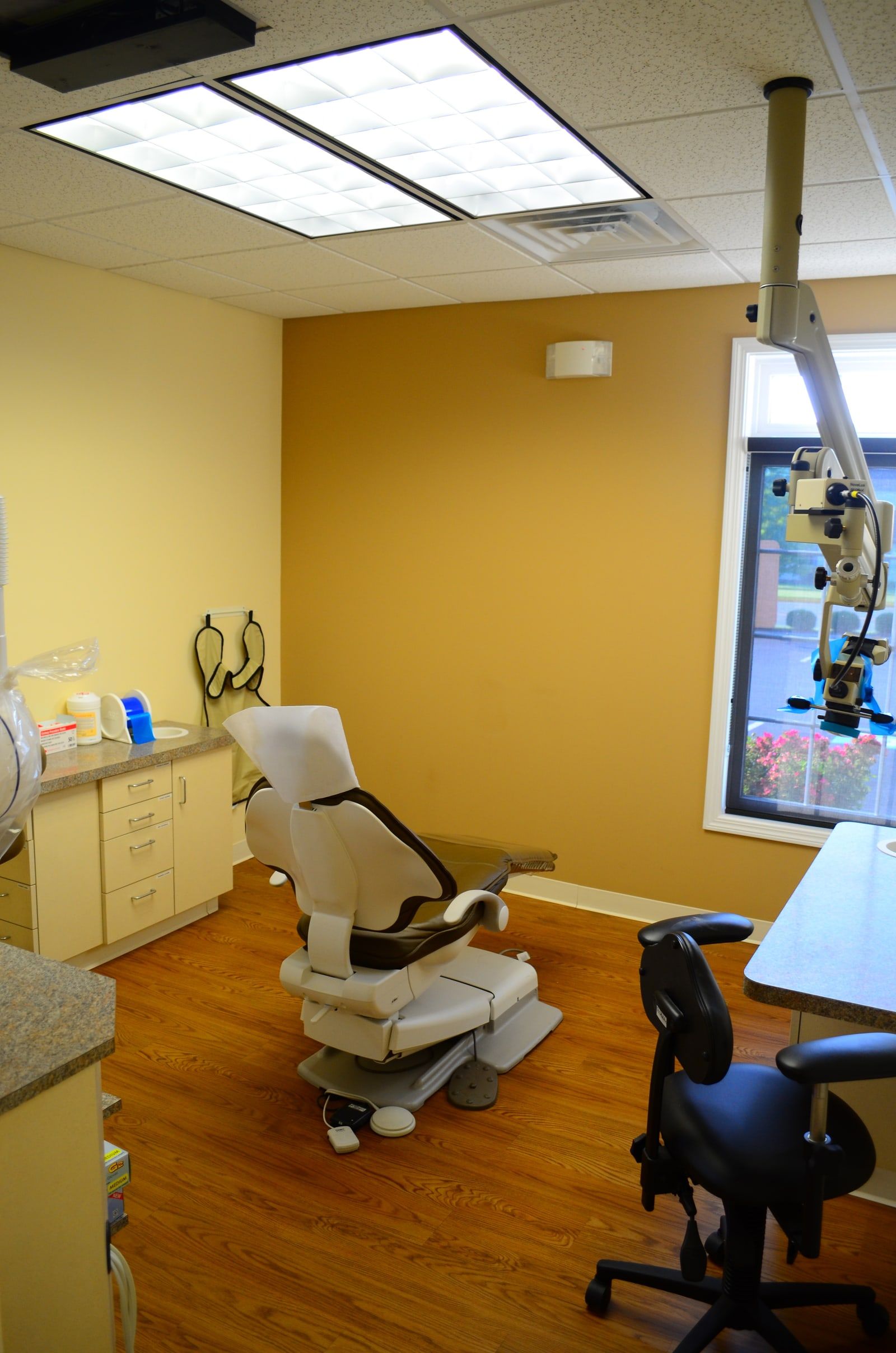 A treatment room with the patient chair and a ceiling-mounted surgical microscope beside the window